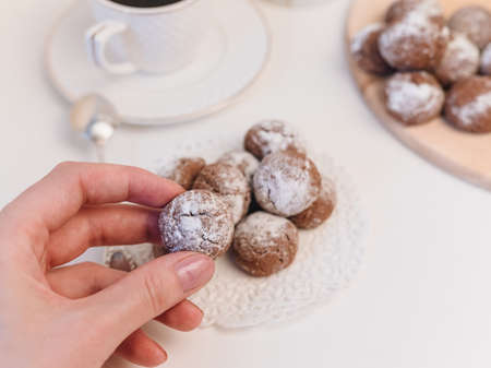 small homemade chocolate chip cookie with powdered sugar in hand close-up, espresso coffee in white cupの写真素材