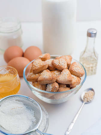 heart shaped shortbread cookies with sesame seeds on a white table, flour, eggs, milk, vegetable oil, honey and sugarの写真素材