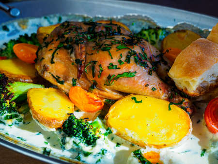 chicken with cilantro, baked in cream with potatoes, broccoli and cherry tomatoes in a metal baking dishの写真素材