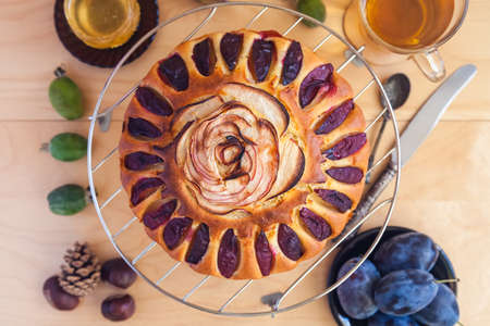 round cake decorated with slices of plums and apples. Autumn still life with fresh fruits and tea on a light wooden tableの写真素材