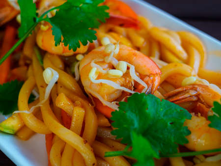 wok with wheat udon noodles, oyster sauce, king prawns, sprouted white mung beans, garnished with sprigs of green cilantro - an Asian dishの写真素材