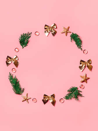 gold bows, twigs of a Christmas tree, beads, stars in the form of a wreath on a peach-colored background. Copy space in center.の写真素材