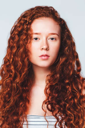 portrait of beautiful red-haired girl with long curly hair on a blue background in the studioの写真素材