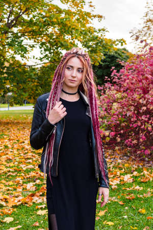beautiful woman with long pink and beige de-dreadlocks in a black jacket and dress looks to the sideの写真素材