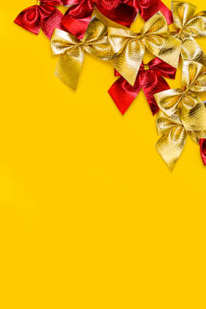 vertical christmas background: red and gold shiny bows on a yellow background. Flat lay, copy space for your textの写真素材