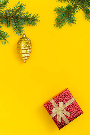 Vertical Christmas yellow background: shiny red gift box, branches of spruce and fir-tree toy - a gold bumpの写真素材
