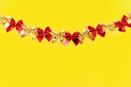 horizontal festive background: shiny red and gold bows on a yellow background - flat lay. Copy space centerの写真素材