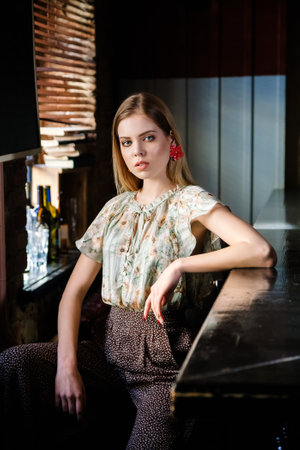 beautiful blonde model sits behind an empty bar counter and looks awayの写真素材