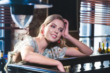 beautiful girl with natural blond hair and blue eyes is sitting at the bar counter and smilingの写真素材