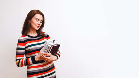 beautiful 30-year-old woman in a striped multicolored dress holds books in her hands. Learning...