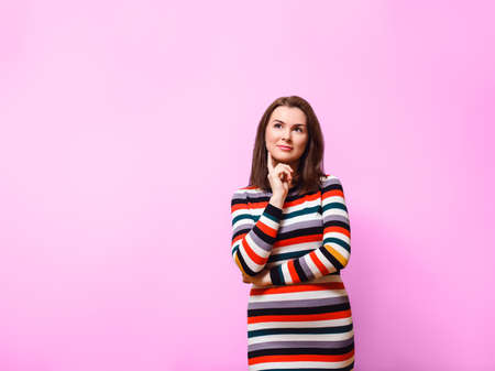 attractive brown-haired woman in multi-colored striped dress smiles and looks to the side. Studio...