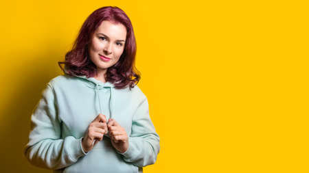 portrait of beautiful young woman in a green hoodie on a yellow background. The model looks into the camera smiling. Studio shot, copy spaceの写真素材