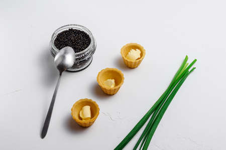 Black caviar in a glass jar with a spoon, three tarts with butter and chives on a white backgroundの写真素材