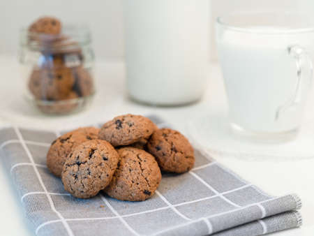 homemade oatmeal cookies with cracks and pieces of chocolate on a gray napkin, a cup of milk and a glass bottle - breakfastの写真素材