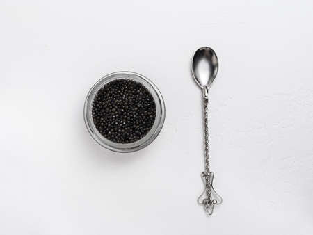 glass jar with black sturgeon caviar and vintage spoon on white background - flatlayの写真素材