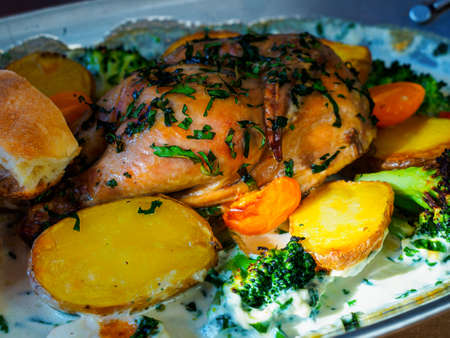 Chicken baked in cream. Vegetables on a metal tray: red and yellow cherry tomatoes, potatoes, broccoli, cilantroの写真素材