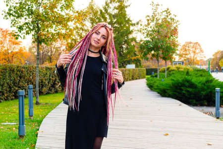 beautiful model with long dreadlocks and pigtails in black clothes walks in the park. Portrait of an attractive young woman outdoors, retouchedの写真素材