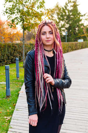 beautiful caucasian woman with pink dreadlocks in black clothes in the park in autumn. Portrait of attractive model, skin retouchingの写真素材