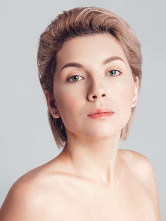 portrait of a beautiful blonde with short hair and green eyes on a gray background. Makeup nude, skin retouchingの写真素材