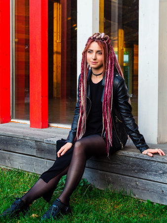 portrait of a beautiful young woman with long dreadlocks and pigtails in black clothes outdoorsの写真素材