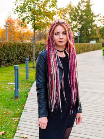beautiful model with long pink and beige dreadlocks and pigtails in black dress and leather jacket in a park in early fall. Attractive woman looking at the cameraの写真素材