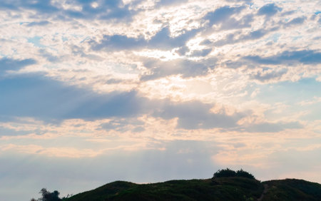 the sun's rays shine from behind the clouds over the hillの写真素材
