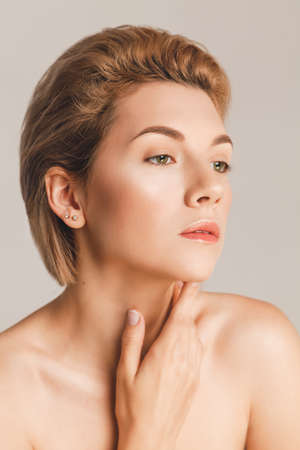 beautiful woman put her hand on her neck and looks away, closeup. Studio shot on a beige background, skin retouchingの写真素材