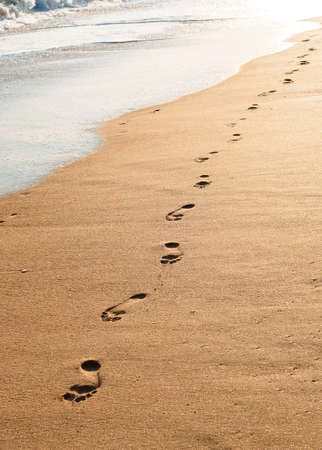 footprints on wet sand on the coastline at sunsetの写真素材