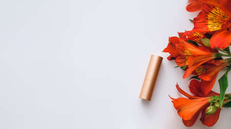 nude lipstick in a golden metal case and a bouquet of red alstroemeria on a white background - flatley, copy spaceの写真素材
