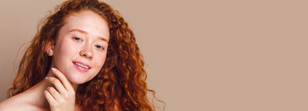 close-up portrait of a beautiful smiling girl with long curly red hair looks on a beige background. No makeup, no retouching, copy spaceの写真素材
