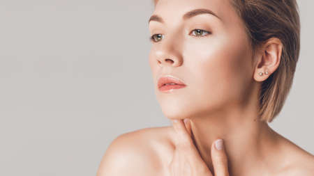 beautiful woman put her hand on her neck and looks away, closeup. Studio shot on a beige background, skin retouchingの写真素材