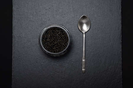 black sturgeon caviar in a glass jar and a silver teaspoon on a slate plate - flatleyの写真素材