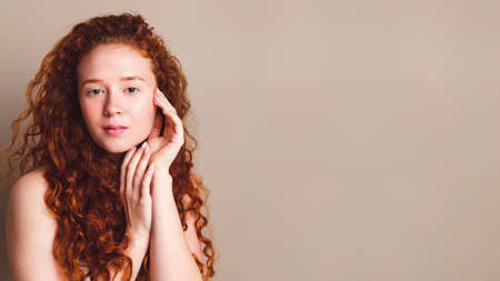 portrait of smiling girl with long curly red hair in the studio on a beige backgroundの写真素材