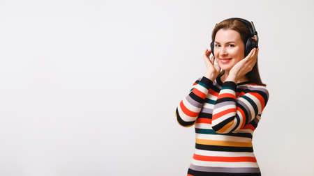 beautiful woman listens to music in isodynamic full-size closed wireless headphones, looks into the camera and smiles. Copy space to the rightの写真素材