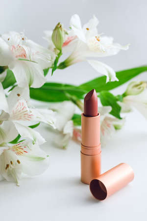 lipstick in a dark red shade in a golden case against a background of white alstroemeriasの写真素材