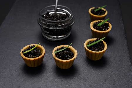 a traditional Russian dish - tartlets with black beluga caviar, decorated with green onion feathersの写真素材