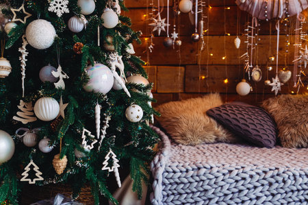 A Christmas tree decorated with white and beige toys and a sofa with a blanket and pillows - a cozy festive atmosphereの写真素材