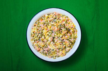 traditional festive dish of Russian cuisine - olivier salad in a large white bowl on a green backgroundの写真素材