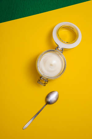 homemade mayonnaise in a glass jar with a sealed lid on a yellow-green background, top viewの写真素材