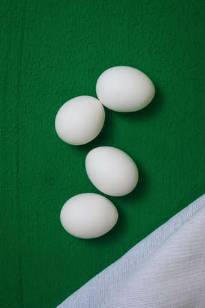 four white chicken eggs and a waffle dishcloth on a green backgroundの写真素材