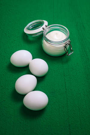 four white chicken eggs and mayonnaise in a glass jar on a green backgroundの写真素材