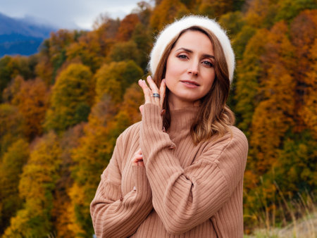 beautiful young woman in a beige suit and an angora beret in autumn in the mountainsの写真素材