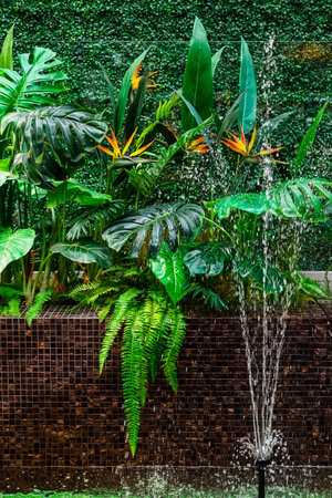 A bush of artificial tropical plants and a fountain as part of an interior design decoration. Plastic realistic leaves and flowers.の写真素材