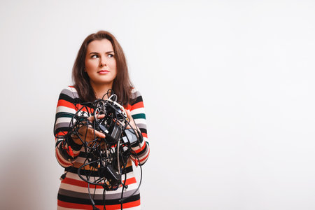 cute woman holding many different wires and looking confused, white background and copy spaceの写真素材