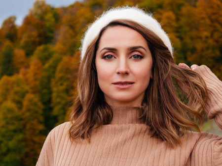 close-up portrait of attractive caucasian woman on a background of mountains in autumn. Blonde model with big beautiful eyes in beige angora beret looks at the cameraの写真素材