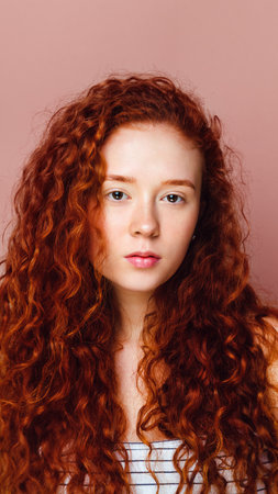 portrait of a cute curly girl on a pink background. Beautiful long red hair, no makeupの写真素材