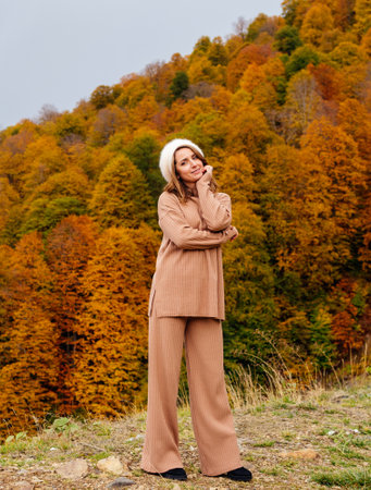 beautiful smiling woman in beige ribbed suit and beret against the backdrop of autumn forest in the mountains. No plastic surgery, no retouchingの写真素材