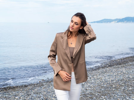 beautiful woman in brown jacket and top walks along the beach in spring and looks awayの写真素材