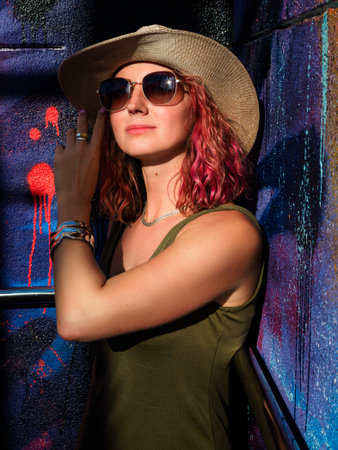beautiful slender woman with curly pink hair in straw hat and sunglasses poses on colorful backgroundの写真素材