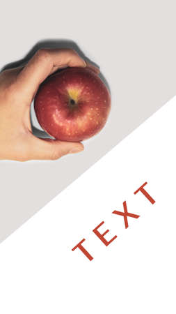 In hand a red apple on a white table. The photo shows a woman's hand holding a ripe red apple.